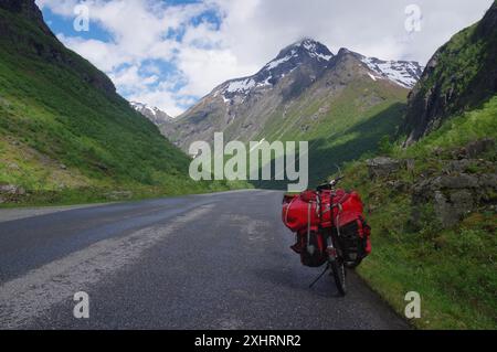Una bicicletta rossa si trova su una strada vuota circondata da verdi montagne e da un paesaggio naturale in una giornata con cielo blu e nuvole, Noerangsdalen, Western Foto Stock
