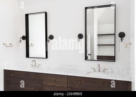 Un bagno di lusso con armadietto di legno scuro, ripiano in marmo e luci a lucernario intorno agli specchi quadrati. Foto Stock