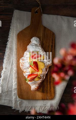 Croissant gourmet appena sfornato, con fragole e crema. Sfondo di legno scuro. Foto Stock