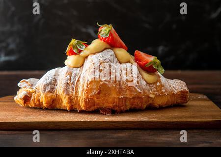 Croissant gourmet appena sfornato, con fragole e crema. Sfondo di legno scuro. Foto Stock