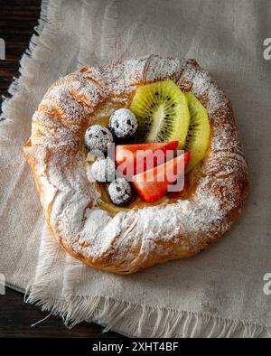 Pasticceria danese appena sfornata con marmellata e frutta. Sfondo di legno scuro. Foto Stock