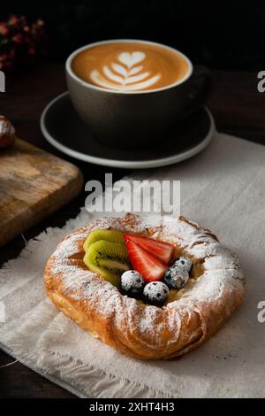 Pasticceria danese con frutta e una tazza di cappuccino. Sfondo scuro. Foto Stock