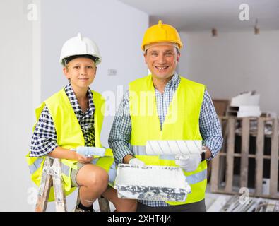 Sorridente ragazzo e padre che tiene rulli di vernice, lavori di miglioramento domestico Foto Stock