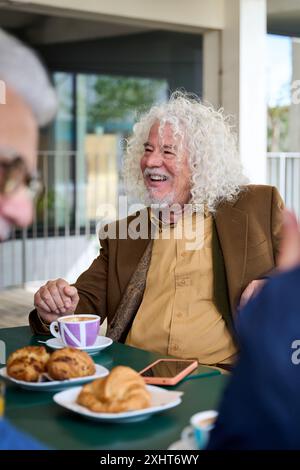 Uomo dai capelli grigi maturo sorridente gustando un caffè con gli amici di gruppo sulla terrazza di casa degli anziani. Foto Stock