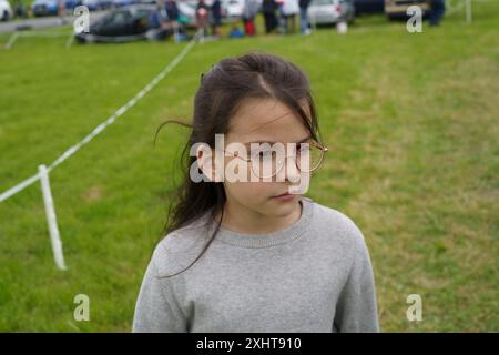 Piccola studentessa che indossa gli occhiali su uno sfondo di erba verde. Concetto di viaggio per bambini Foto Stock