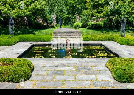 Bronx, New York - US - 13 luglio 2024 la fontana quadrata sommersa della Bartow–Pell Mansion presenta un'affascinante statua di cherubino circondata da gigli, incorniciata da m. Foto Stock