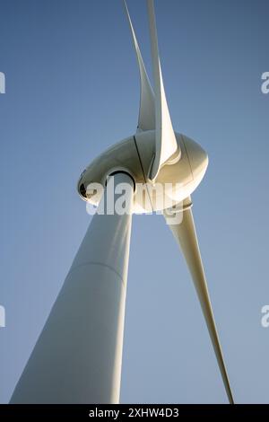 Questa immagine cattura una vista ravvicinata e ad angolo basso di una moderna turbina eolica posizionata contro un cielo azzurro. Il design elegante e aerodinamico della turbina b Foto Stock