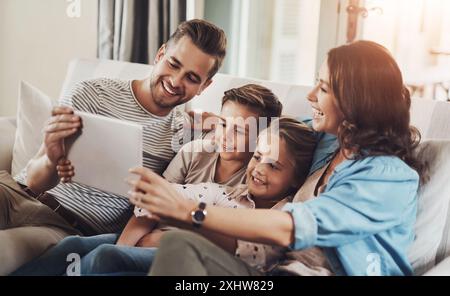Genitori, bambini e felici con un tablet sul divano per giochi didattici, cartoni animati e intrattenimento. Persone, famiglia e sorridi sul divano in salotto con divertimento Foto Stock
