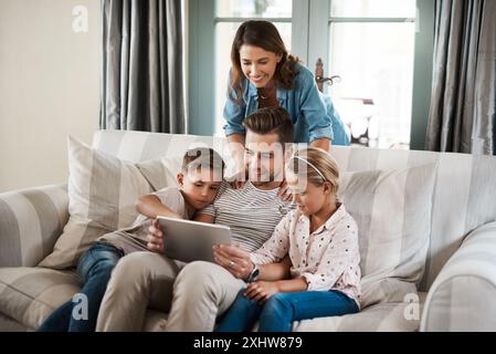 Genitori, bambini e felici con un tablet a casa sul divano per giochi didattici, cartoni animati e intrattenimento. Persone, famiglia e sorrisi sul divano in soggiorno Foto Stock