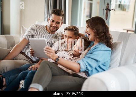 Genitori, bambini e sorrisi con un tablet sul divano per giochi didattici, cartoni animati e intrattenimento. Persone, famiglia e felici sul divano in soggiorno con divertimento Foto Stock