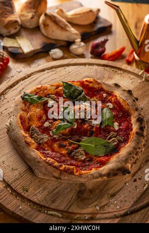 Tradizionale pizza italiana con salsa di pomodoro, aglio, basilico e origano su un asse di legno Foto Stock