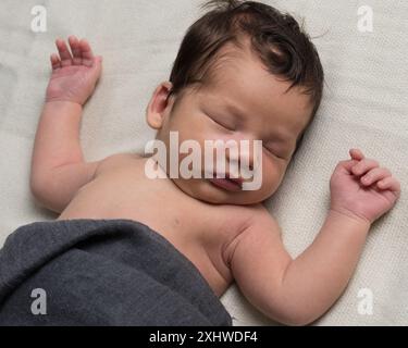 Neonato nei primi giorni di vita. Un bambino appena nato giace su una coperta bianca, avvolta da una coperta grigia. Foto Stock