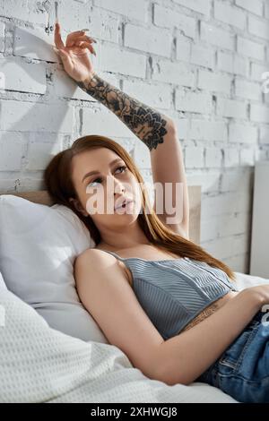 Una giovane donna con i tatuaggi si rilassa su un letto in un appartamento moderno, godendosi un fine settimana accogliente. Foto Stock