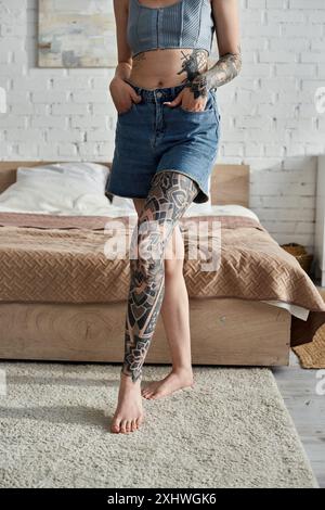 Una giovane donna con i tatuaggi si trova nel suo appartamento moderno, godendo di un fine settimana accogliente a casa. Foto Stock