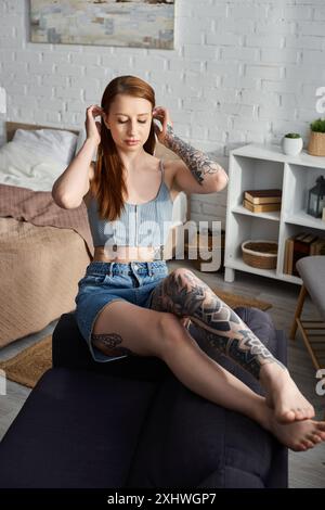 Una giovane donna con i tatuaggi si rilassa su un divano in un appartamento moderno. Foto Stock