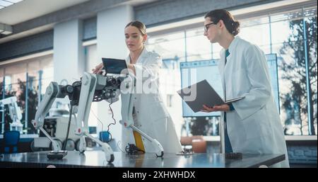 Il Project Manager maschio e l'operatore di macchinari femminile collaborano a un progetto animale robot mobile, utilizzando un computer portatile. Due ingegneri professionisti che discutono di un animale domestico futuristico Foto Stock