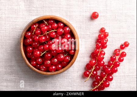 Bacche di ribes rosso, ribes rosso fresco maturo e crudo in una ciotola di legno su tessuto di lino. Pronti a mangiare frutti commestibili sferici di Ribes rubrum. Foto Stock