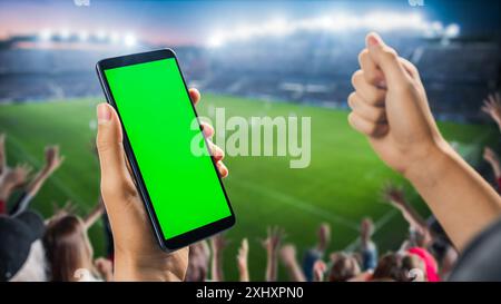 Campionato internazionale di calcio sullo stadio: Fan su Tribune Holding smartphone con schermo verde Chromakey, acclamazione per la squadra preferita. Modello Copyspace per primi piani POV isolato Foto Stock