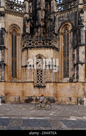 Il ragazzo con un casco rosso spinge la sua bici di fronte alla facciata gotica del monastero di Batalha Foto Stock