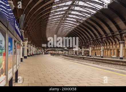 Una piattaforma della stazione ferroviaria, fiancheggiata da colonne, curva in lontananza. Una storica tettoia del XIX secolo è sopraelevata e una passerella pedonale collega il piano Foto Stock