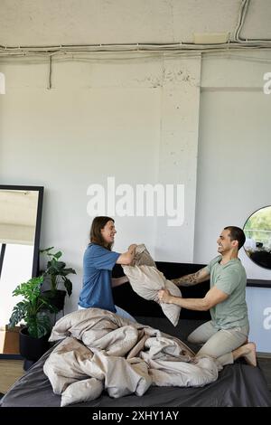 Due giovani si impegnano giocosamente in una lotta con i cuscini in una camera da letto moderna, mostrando la loro relazione amorosa. Foto Stock