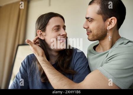 Una giovane coppia gay condivide un momento tenero nella loro camera da letto, guardandosi negli occhi. Foto Stock