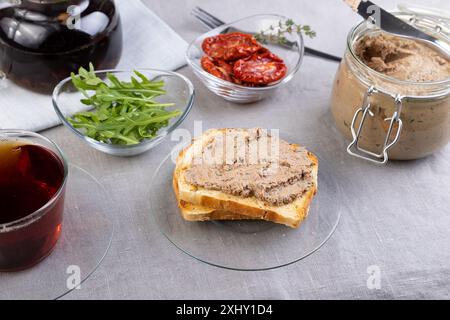 Pate di fegato di pollo con pane di grano, rucola, pomodori secchi e tè nero. Cucina rustica tradizionale fatta in casa. Opzione colazione o spuntino. Selezionare Foto Stock