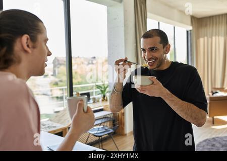 Una giovane coppia gay gode di una colazione rilassata insieme nella loro casa moderna. Foto Stock