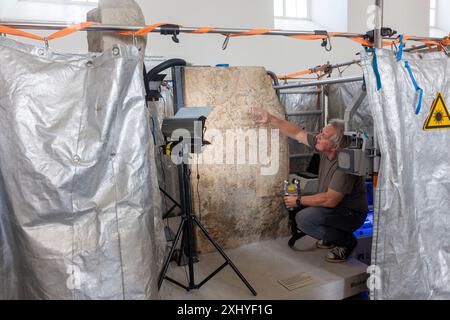 Mainz, Germania. 16 luglio 2024. Il restauratore Mathias Steyer lavora sulla cosiddetta "pietra Blussus", una lapide dell'epoca romana. La lapide di un Celto, raffigurata con sua moglie Menimane su un lato della pietra e mostra un'iscrizione e una raffigurazione di una nave del i secolo dall'altro lato, è stata trovata a Mainz-Weisenau. Credito: Helmut Fricke/dpa/Alamy Live News Foto Stock