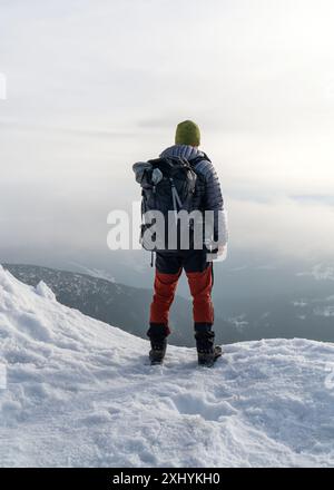 Persone attive in natura. Un turista maschile si trova ai margini di una montagna e gode della vista mentre cammina attraverso le montagne innevate. Sniezka ( Foto Stock