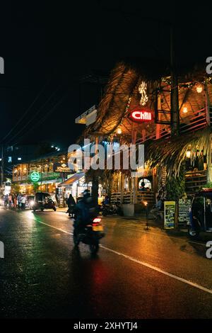 Scena notturna di una strada vivace con luci al neon colorate e gente che passeggia davanti a vivaci ristoranti e caffetterie Foto Stock