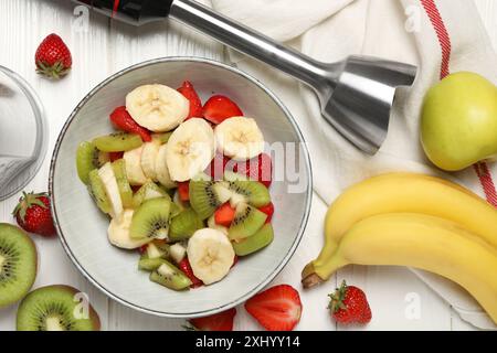 Kit frullatore a immersione, frutta fresca e fragole nel recipiente su un tavolo di legno bianco, piatto Foto Stock