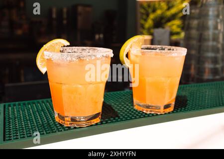 Due bicchieri con cocktail agli agrumi al bar. Deliziose bevande ghiacciate con fette di limone. Succo d'arancia fresco sul tavolo in un caffè all'aperto Foto Stock