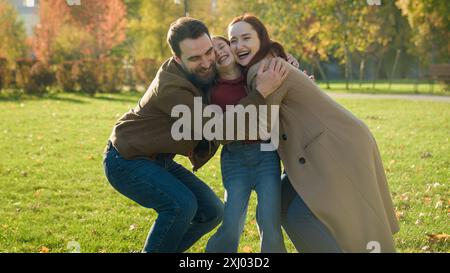 Famiglia caucasica felice amorevole padre madre genitori con figlia bambina bambina ragazza abbracciare sorridere abbracciare insieme coccolare abbracciare abbracciare al sole Foto Stock