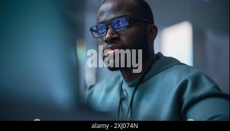 Primo piano Ritratto di Black Man che lavora al computer, Lines of Code Language che riflette sui suoi occhiali. Programmatore maschile che sviluppa nuovo software, Managing Cybersecurity Defence Project. Foto Stock