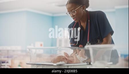 Reparto dell'ospedale di maternità: Infermiera cordiale della testa nera che si prende cura di un neonato. Pediatra africana che rimette il bambino nel Bassinetto durante un Checkup in Nursery Foto Stock