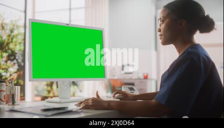 Ritratto di un professionista di sanità medica femminile nero che lavora sul computer desktop con schermo verde Mock Up display in ufficio ospedaliero. Il capo infermiere della clinica sta nominando le prescrizioni online Foto Stock