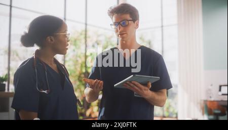 Ospedale medico di assistenza sanitaria. Infermiera afroamericana felice e un medico che ha una conversazione informale, che usa il computer tablet, ridendo e sorridendo durante una pausa al lavoro Foto Stock
