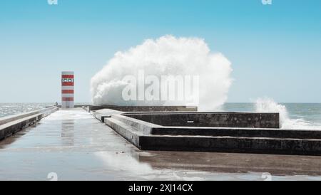 Onde che si schiantano contro il faro sulla frangiflutti. Faro a strisce rosse e bianche alla foce del fiume Douro a Foz do Douro vicino a Porto. Foto Stock