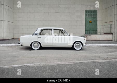 Vecchia berlina bianca di fronte al muro dell'edificio piastrellato in avorio. Vista laterale del profilo della Lada 2101 degli anni '1970 (nota anche come Fiat 124), un'auto d'epoca abbassata. Foto Stock