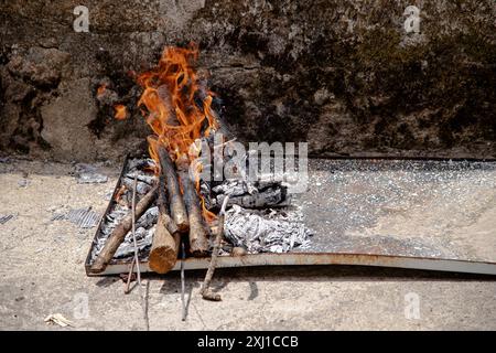 Una piccola fossa antincendio all'aperto si illumina di tronchi e accensioni, collocata contro un rustico muro di pietra Foto Stock