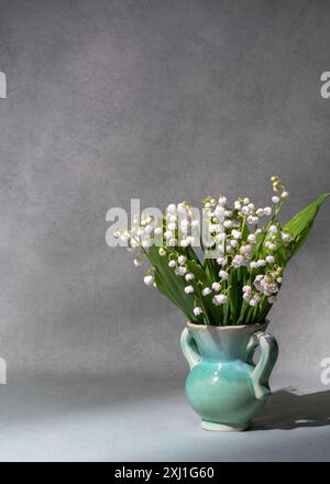 Un piccolo bouquet di freschi fiori primaverili. Gigli della valle in un vaso chiaro isolato su sfondo grigio. Molto spazio per il testo. natura morta, postco Foto Stock