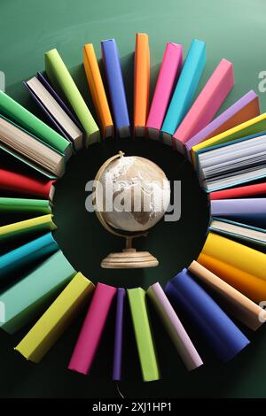Globo circondato da molti libri colorati su sfondo verde, pianeggiante Foto Stock