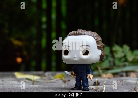 Funko Pop action figure del serial killer Michael Myers dei film horror Halloween. Cortile scuro, recinzione nera, ombre, sfondo verde umido. Foto Stock