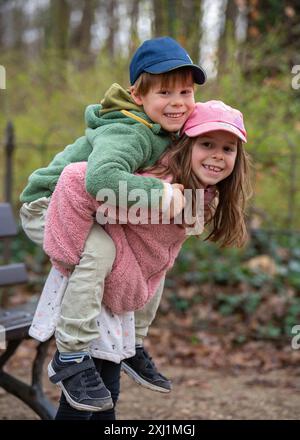 Carini fratello e sorella che si divertono all'aperto. Una ragazza tiene un bambino sulla schiena. Giochi divertenti in natura. Un'infanzia felice e gioiosa Foto Stock