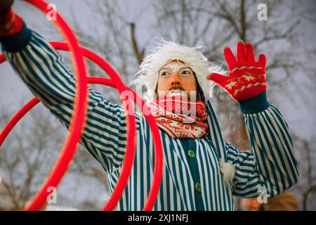 Un clown con una tuta a righe gli fa ruotare dei cerchi rossi sul braccio Foto Stock