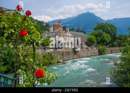 Merano, Südtirol, Italien - Kurhaus am Fluss Passer, an der Passerpromenade in der Altstadt. Vorne Rote Rosen auf der Thermenbrücke. Merano Süddtirol Italien *** Merano, alto Adige, Italy Spa House sul fiume Passer, sul lungomare di Passer nel centro storico Rose rosse di fronte al ponte termale Merano alto Adige Italia Foto Stock