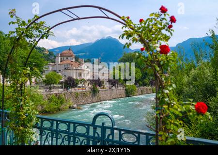 Merano, Südtirol, Italien - Kurhaus am Fluss Passer, an der Passerpromenade in der Altstadt. Vorne Rote Rosen auf der Thermenbrücke. Merano Süddtirol Italien *** Merano, alto Adige, Italy Spa House sul fiume Passer, sul lungomare di Passer nel centro storico Rose rosse di fronte al ponte termale Merano alto Adige Italia Foto Stock