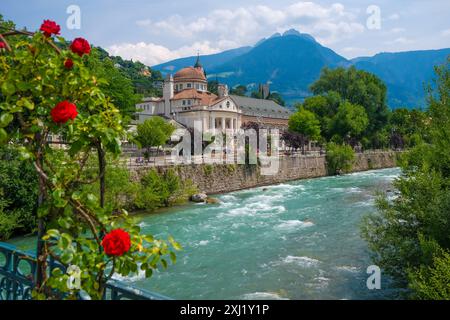 Merano, Südtirol, Italien - Kurhaus am Fluss Passer, an der Passerpromenade in der Altstadt. Vorne Rote Rosen auf der Thermenbrücke. Merano Süddtirol Italien *** Merano, alto Adige, Italy Spa House sul fiume Passer, sul lungomare di Passer nel centro storico Rose rosse di fronte al ponte termale Merano alto Adige Italia Foto Stock