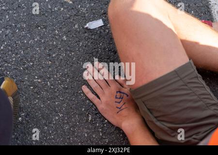 15 luglio 2024, Varsavia, Polonia: Un attivista con l'iscrizione "colla" tiene la mano incollata alla strada durante la dimostrazione. Le persone in giubbotti arancioni (attivisti dell'ultima generazione) hanno bloccato il traffico su Aleja Jana Pawla II. Si tratta di attivisti dell'ultima generazione che chiedono investimenti nel trasporto pubblico. L'ultima generazione ha bloccato le principali arterie di Varsavia per la terza settimana. L’ultima generazione ha dichiarato davanti alle telecamere: Non ci fermiamo, il nostro obiettivo è la più lunga serie di azioni di resistenza civile contro il crollo climatico in Polonia. Nella stagione piu' calda, la gente si sveglia Foto Stock